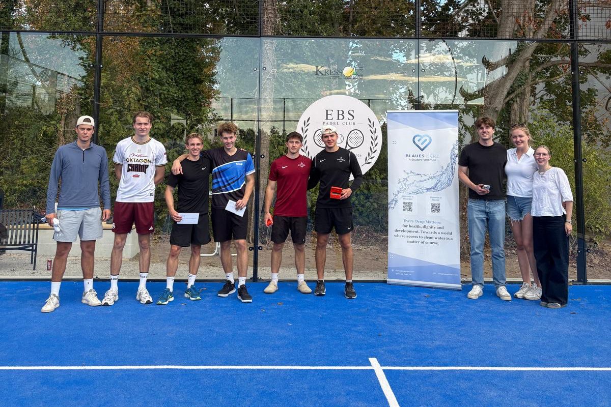 Gruppenfoto nach dem Charity-Padel-Turnier auf dem Court des EBS Padel Club, daneben der Aufsteller von Blaues Herz e.V.